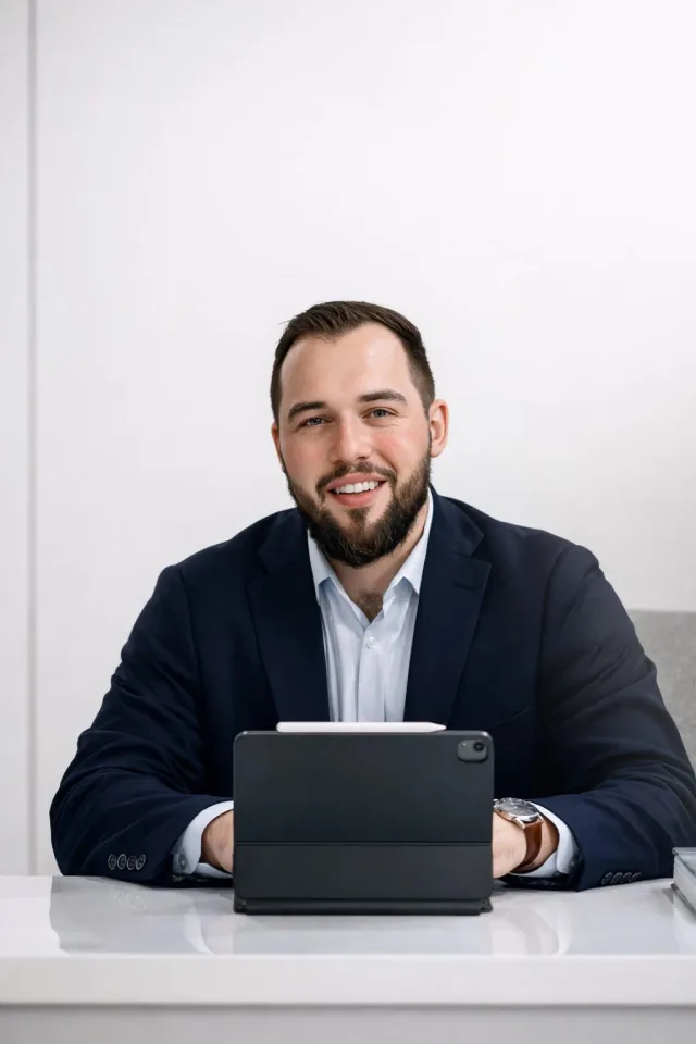 Real estate agent seated at a desk with a tablet, wearing a navy blazer