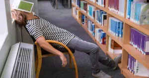 Student asleep in the library with book on his face