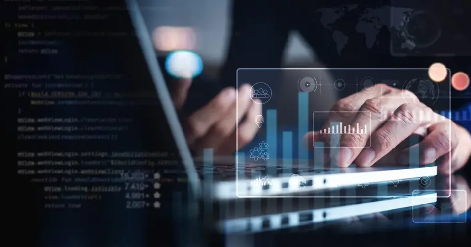 A person using a laptop with digital data visualizations and lines of programming code overlaid on the screen.