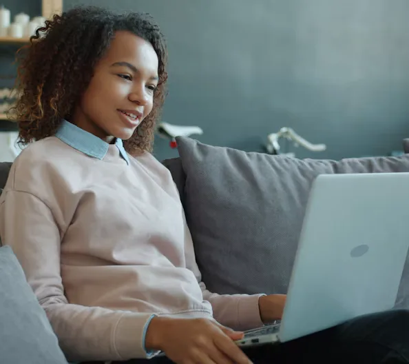 Young woman smiling while using a laptop on the couch.