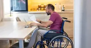 A man in a wheelchair at a table using a laptop and holding papers to demonstrate the issue of inheritance and ODSP benefits.