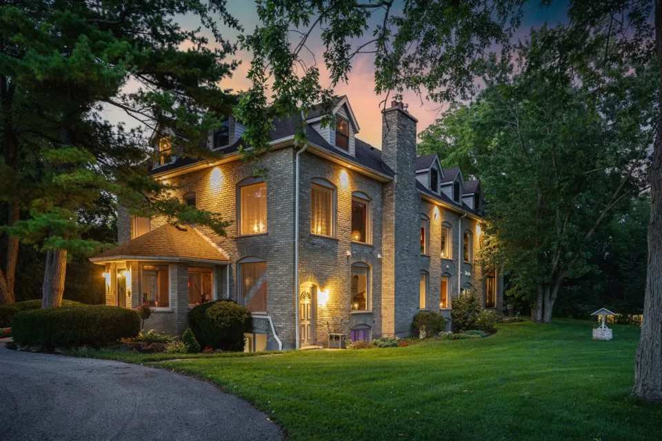Twilight view of Cedarmere Woods, with illuminated windows, mature trees and landscaped grounds
