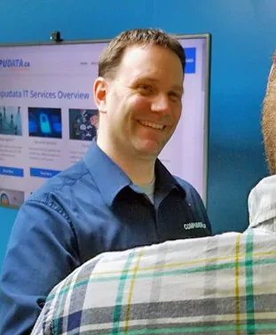 A Compudata staff member smiling in conversation with a client, in front of a screen showing the Compudata IT services overview page